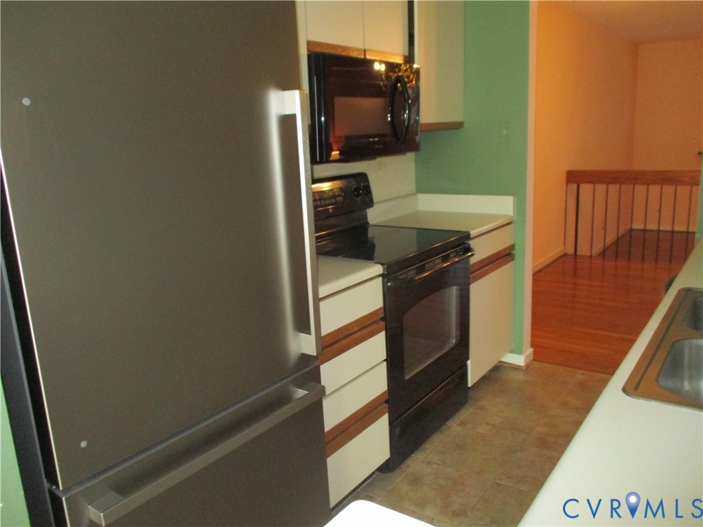 Kitchen featuring a stainless steel refrigerator, black appliance suite, solid-surface countertops, flat-panel cabinetry, and dual-basin sink