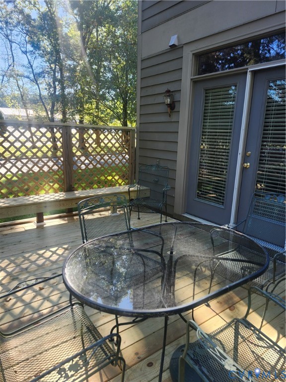 Wood-deck patio featuring a built-in lattice privacy screen, horizontal lap siding, and double glass-panel entry doors with wall-mounted exterior lighting