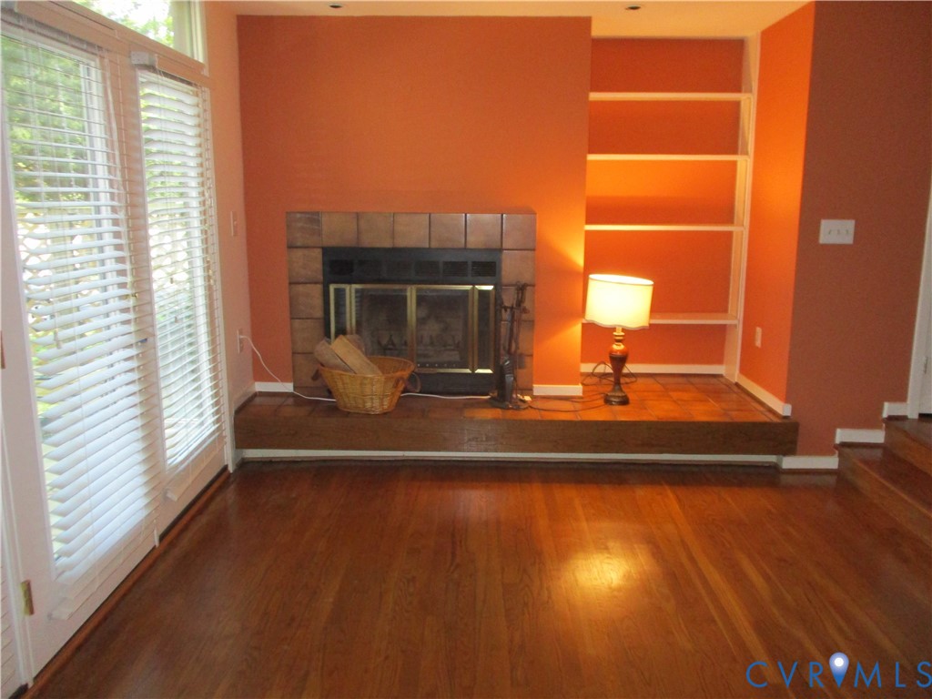 Fireplace with tile surround and raised hearth, hardwood flooring, built-in shelving, and double-glass door entry