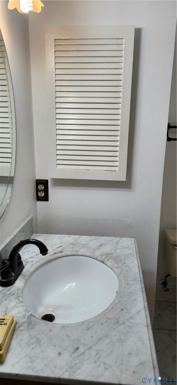 Stone-topped vanity featuring an undermount oval sink, matte black faucet, and louvered wall-mounted storage cabinet
