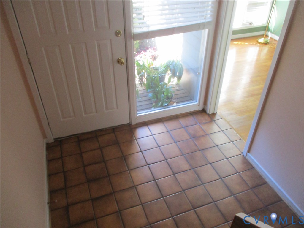 Entryway featuring ceramic tile flooring, a multi-panel door with metallic hardware, and a side light window with horizontal blinds