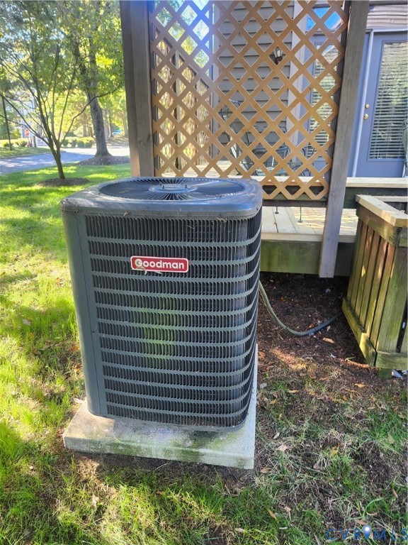 Exterior Goodman condenser unit mounted on a concrete pad, situated near a wood lattice privacy screen and vertical-plank enclosure