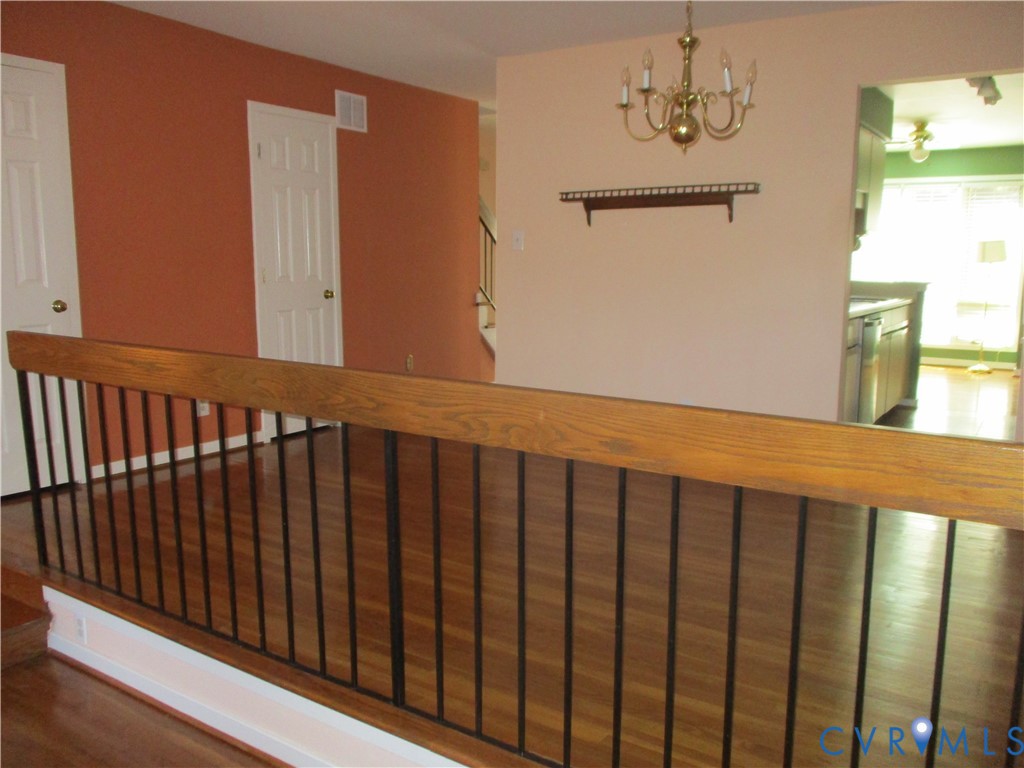 Wood-finish flooring, staircase with a wood handrail and metal balusters, traditional brass-finish chandelier, and wall-mounted wooden display shelf