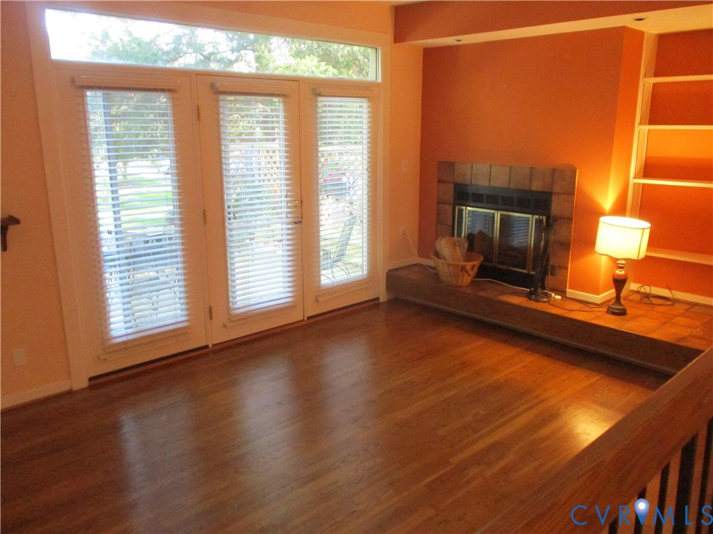 Wood-finish flooring, fireplace with tiled hearth, built-in shelving, and floor-to-ceiling glass panel doors
