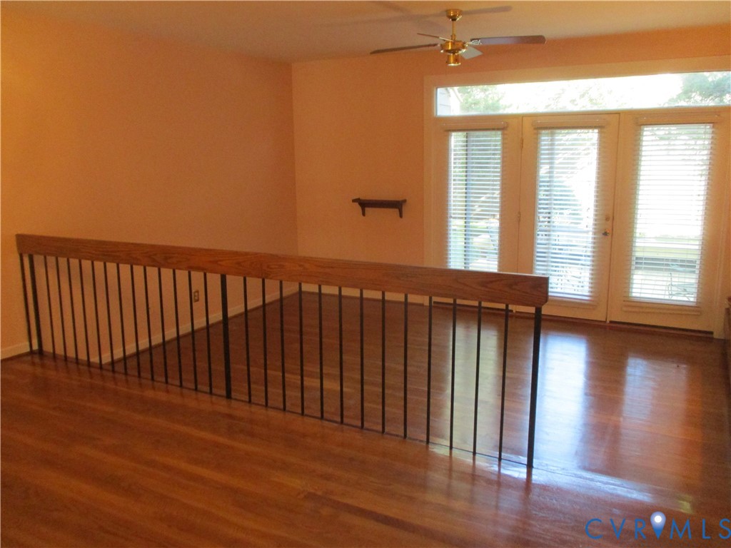 Wood-finish flooring, full-light French doors with integrated transom windows, metal balustrade with a wooden handrail, and a ceiling-mounted fan