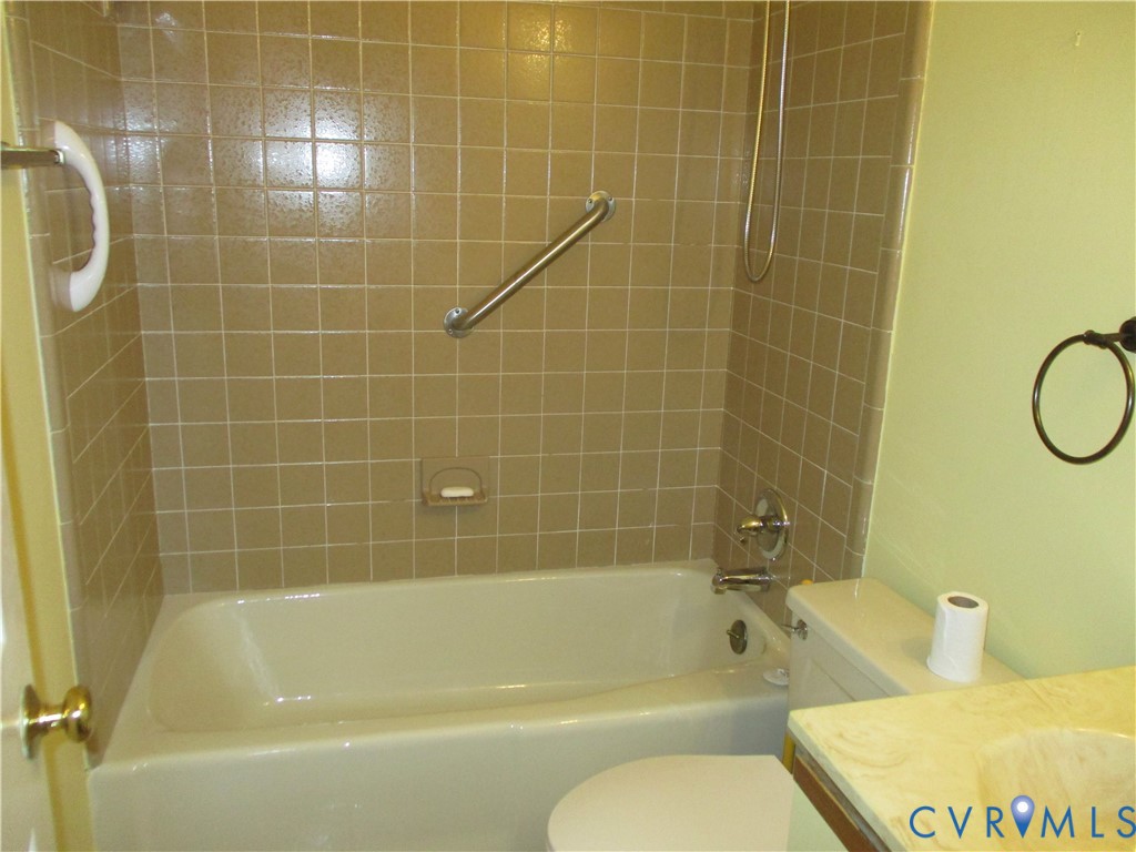Bathtub with ceramic wall tile surround, integrated metal grab bars, wall-mounted shower head, and vanity with integrated basin