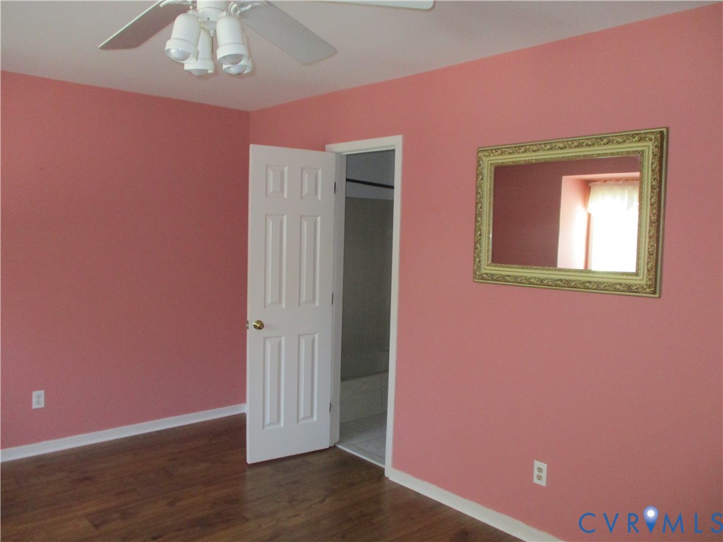 Room featuring wood-finish flooring, a ceiling fan with integrated lighting, and a six-panel interior door