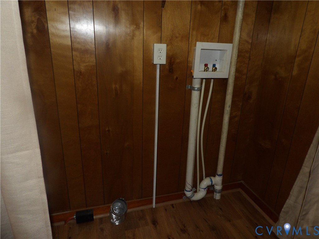 Laundry area featuring wood-finish wall paneling, dedicated water supply lines, drainage plumbing, and a built-in electrical outlet