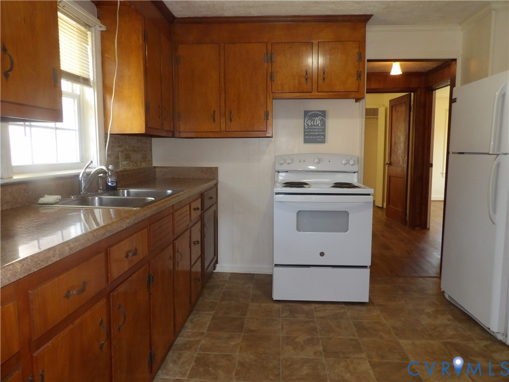 Kitchen featuring wood cabinetry, laminate countertops, double-basin stainless steel sink, and white electric range