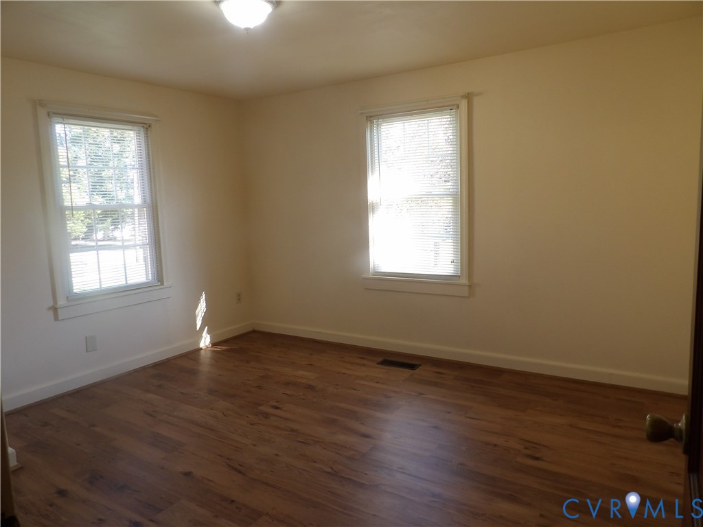 Interior room featuring wood-finish flooring, neutral wall tones, and two windows with horizontal blinds