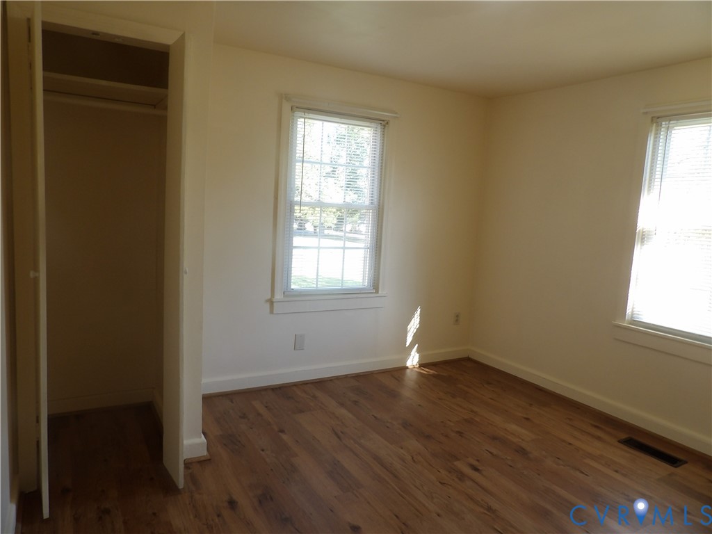 Room featuring wood-finish flooring, two windows with grid muntins, and a built-in closet with overhead shelving