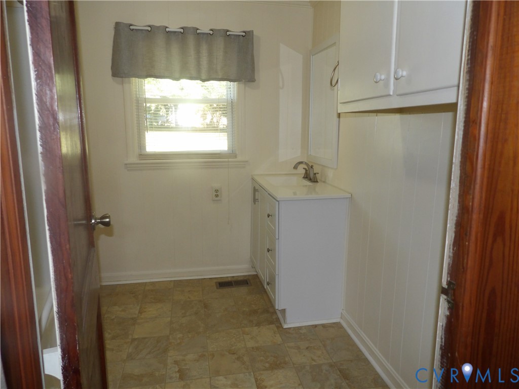 Single-basin vanity with white cabinetry, square-tiled flooring, wall-mounted upper storage, and a multi-pane window