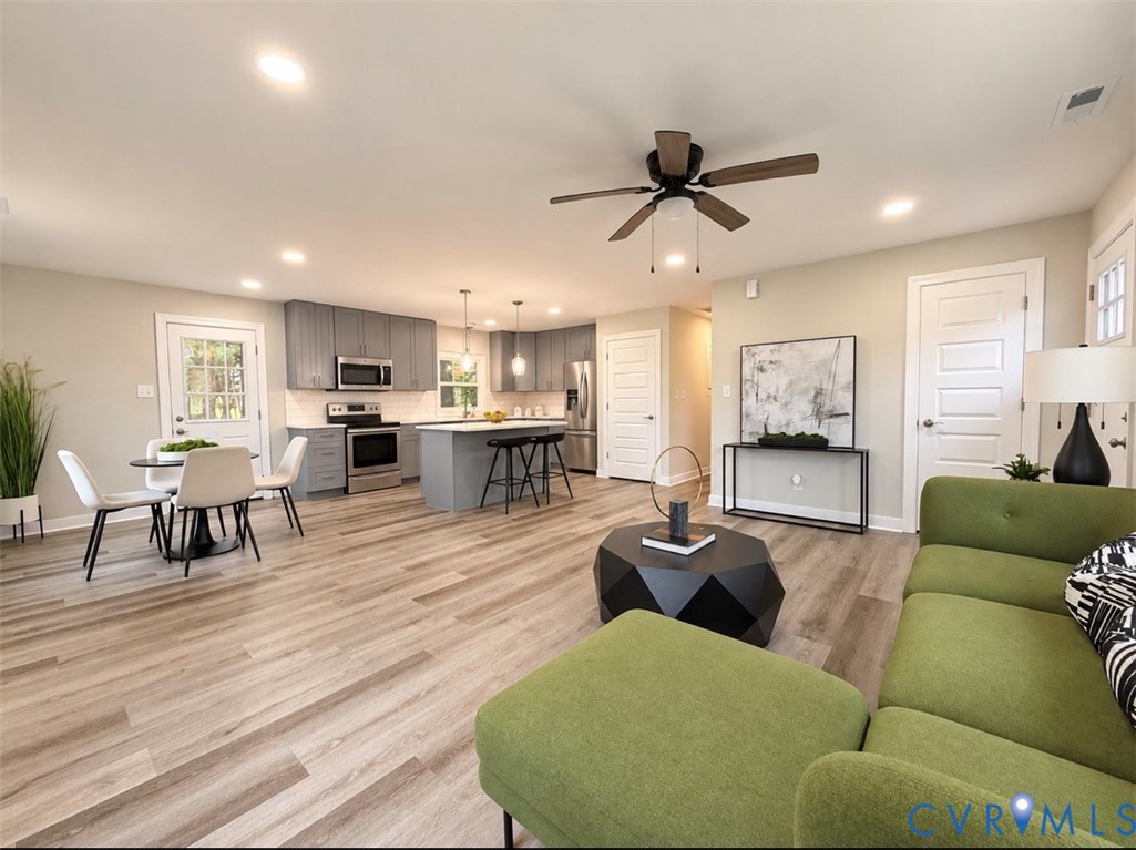 Open floor plan featuring wood-finish flooring, a kitchen with a center island, gray shaker-style cabinetry, stainless steel appliances, and recessed lighting