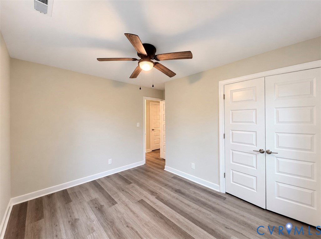 Wood-finish flooring, neutral wall tones, multi-paneled double closet doors with satin nickel hardware, and a center-mounted ceiling fan with integrated lighting