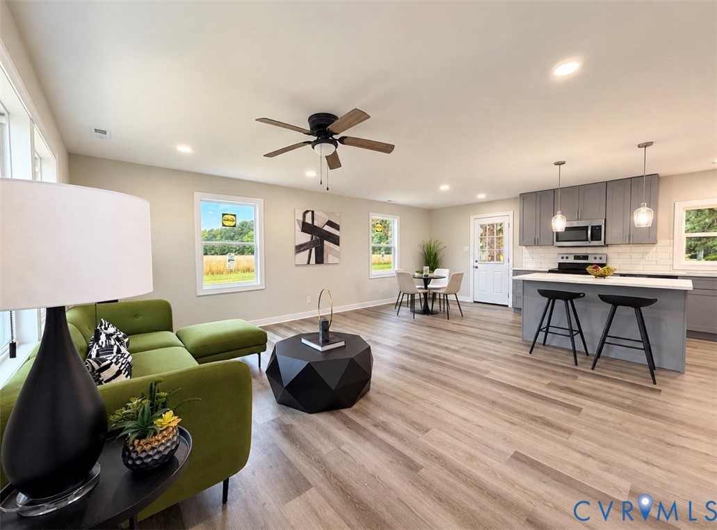 Open-concept interior featuring wood-finish flooring, recessed lighting, and a kitchen equipped with stone-surface countertops, a breakfast bar, and stainless steel appliances