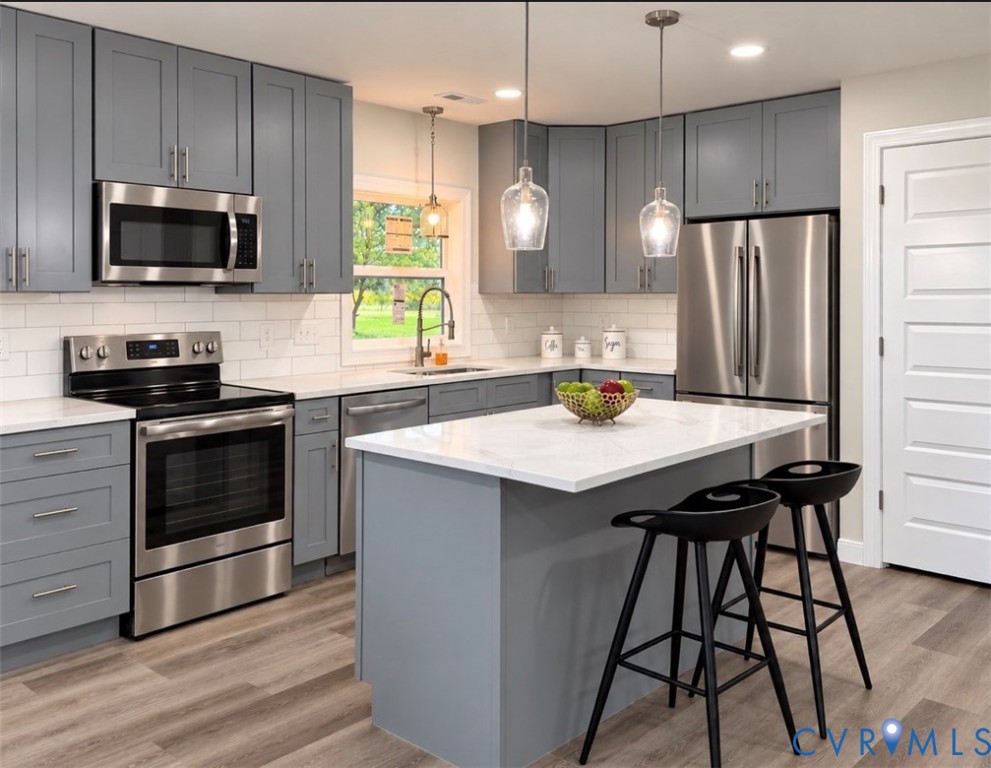 Kitchen featuring slate-colored cabinetry, stone-finish countertops, stainless steel appliances, a central island, and wood-finish flooring
