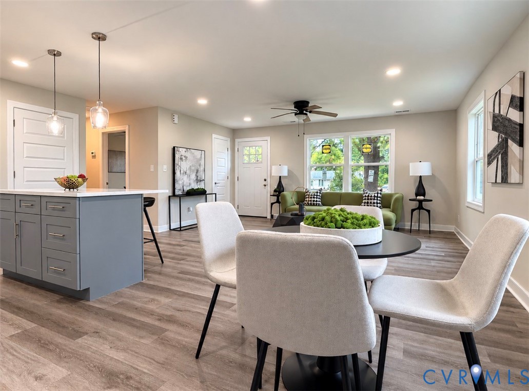 Open-concept interior featuring wood-finish flooring, a kitchen island with gray cabinetry, recessed lighting, dual glass pendant lights, and a central ceiling fan