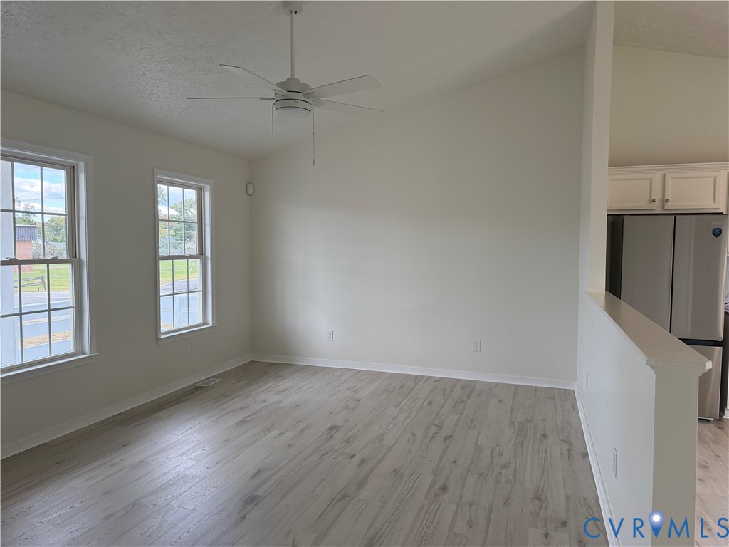 Vaulted ceilings, wood-finish flooring, white cabinetry, dual-pane windows, and a ceiling fan
