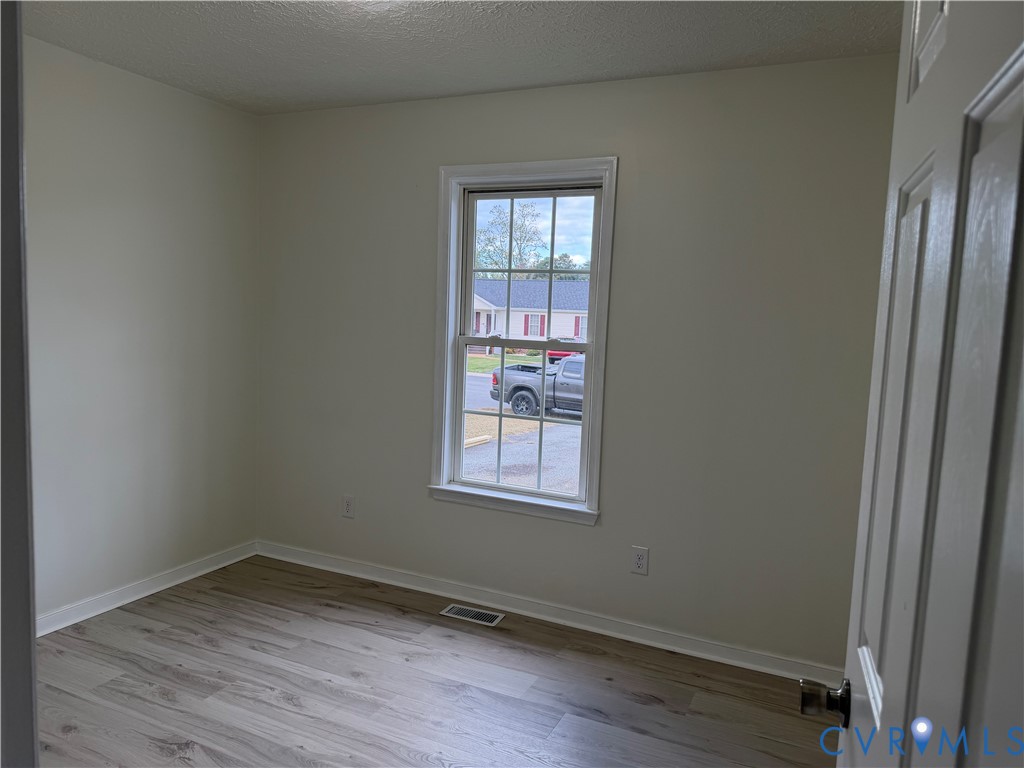 Neutral-toned interior space featuring wood-finish flooring, a single-hung window with a muntin grid, and a classic six-panel door