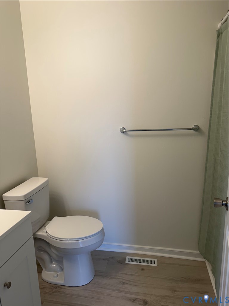 White vanity cabinet, dual-flush toilet, and wall-mounted metal towel bar finished with wood-finish flooring