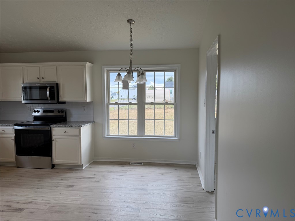 Kitchen featuring off-white cabinetry, stone-finish countertops, stainless steel appliances, wood-finish flooring, and a multi-light chandelier