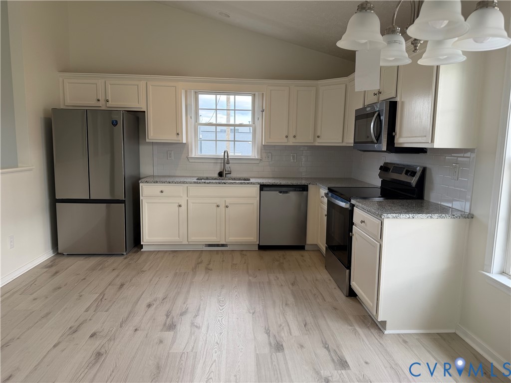 Kitchen featuring white shaker-style cabinetry, stone-finish countertops, stainless steel appliances, a tile backsplash, and light-tone wood-finish flooring