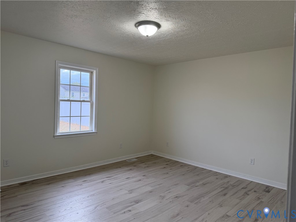 Neutral-toned room with wood-finish flooring, white walls, double-hung grid window, and a flush-mount ceiling light fixture