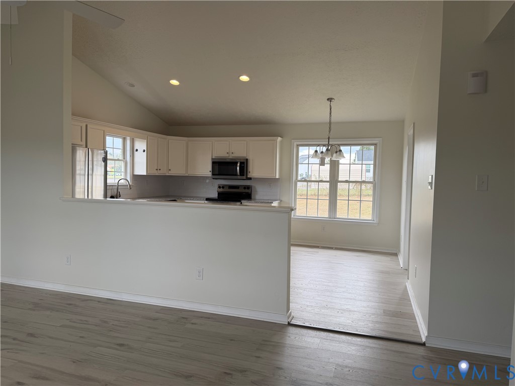 Kitchen featuring white cabinetry, stainless steel appliances, wood-finish flooring, vaulted ceilings, and a multi-light chandelier