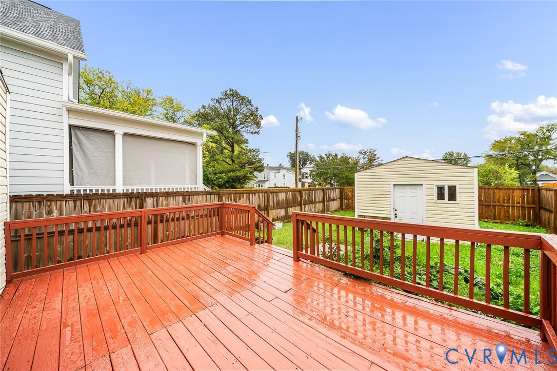 Elevated wood deck featuring protective railings, screened porch, detached storage structure, and fenced perimeter