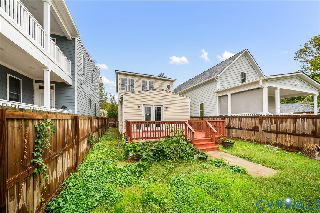 Exterior rear elevation featuring lap siding, double glass-pane doors, an elevated wood deck with railing, and a fenced perimeter