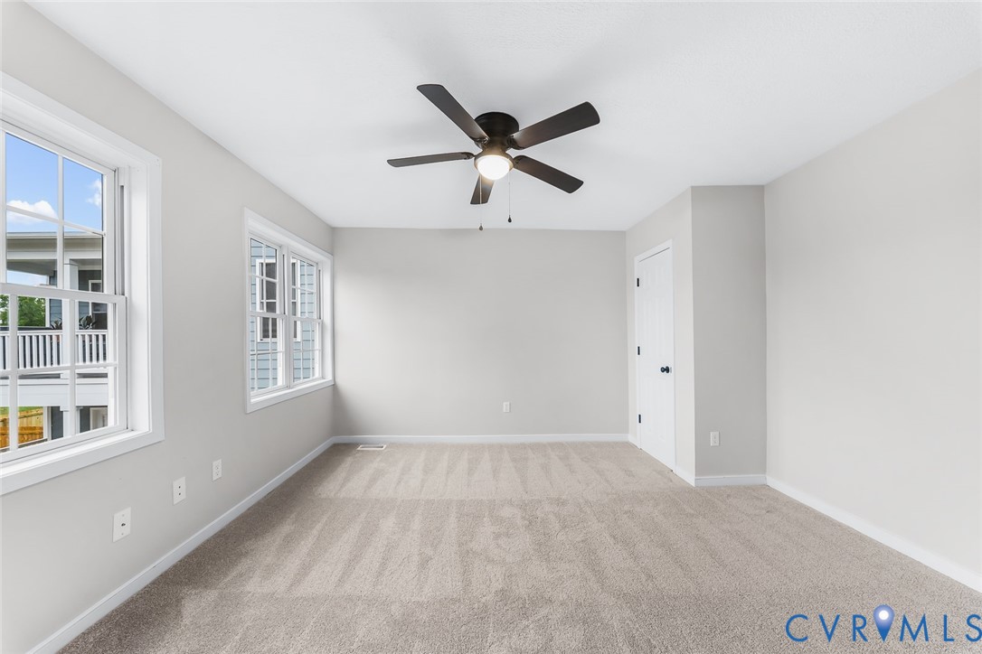 Neutral-toned interior featuring wall-to-wall carpeting, multiple double-hung windows, and a ceiling fan with integrated lighting