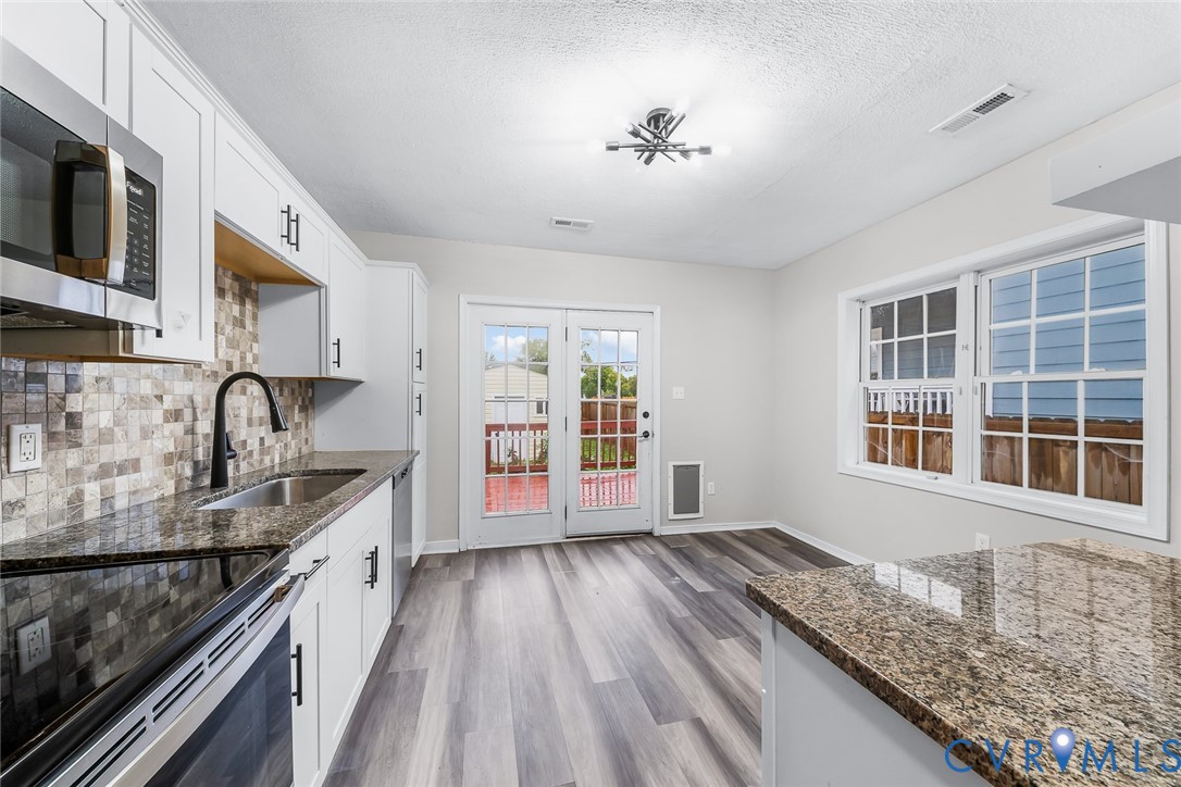 Kitchen featuring white shaker-style cabinetry, stone-finish countertops, mosaic tile backsplash, wood-finish flooring, and double glass-paneled doors