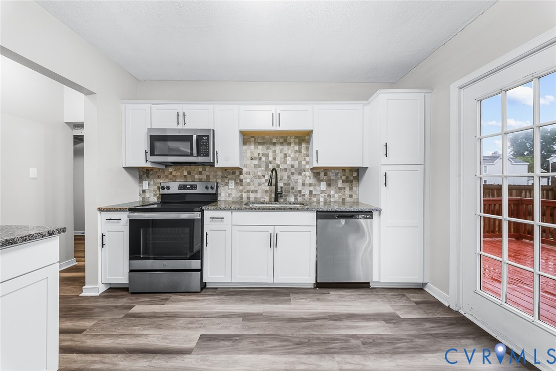 Kitchen featuring white Shaker-style cabinetry, stone-finish countertops, mosaic tile backsplash, stainless steel appliances, and wood-finish flooring