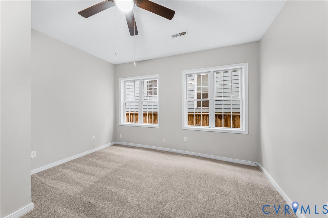 Neutral wall tones, wall-to-wall carpeting, two multi-pane windows with white trim, and a ceiling-mounted light fixture with fan blades
