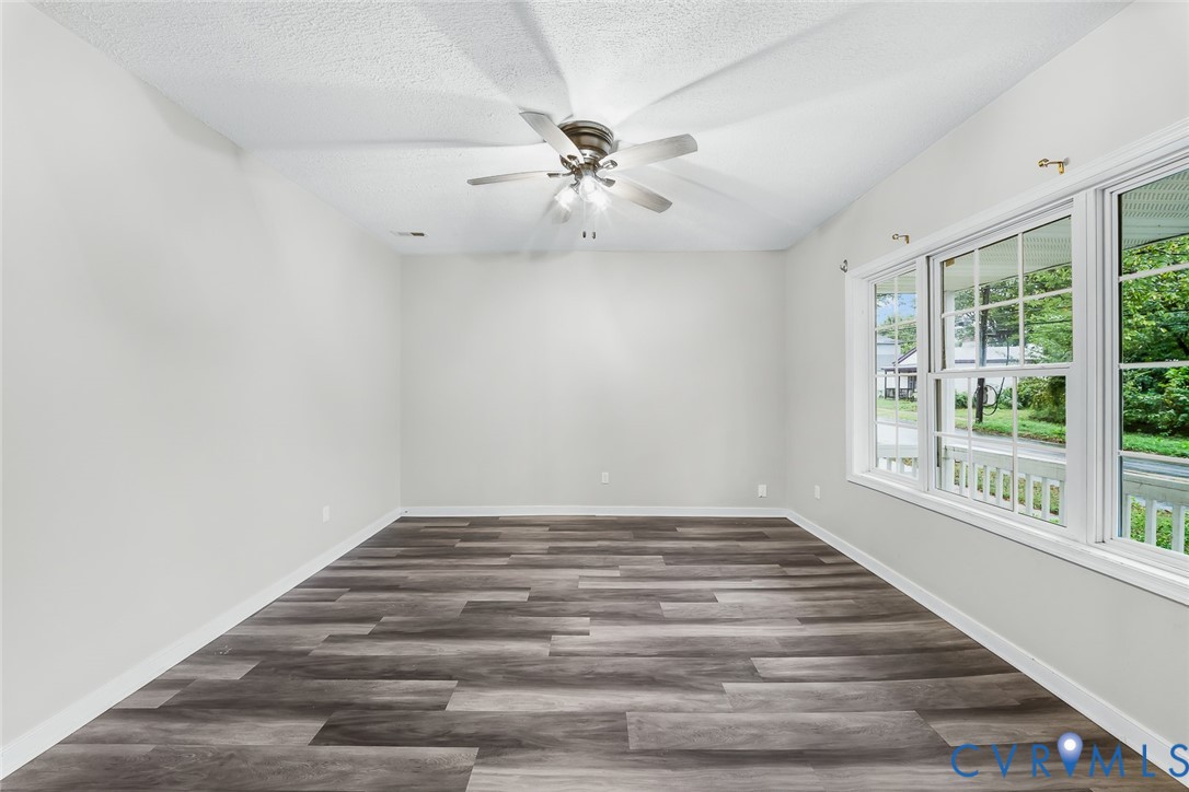 Neutral-toned interior space featuring wood-finish flooring, vaulted ceilings, a ceiling fan with integrated lighting, and expansive windows