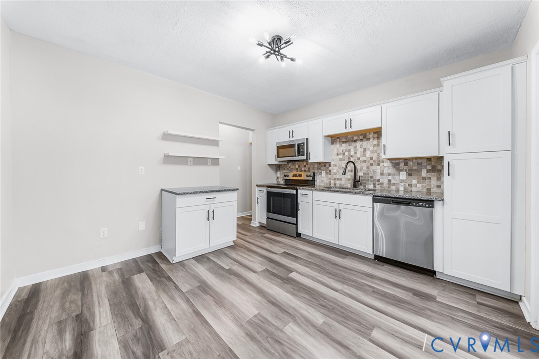 Kitchen featuring white shaker-style cabinetry, multi-toned tile backsplash, stone-finish countertops, stainless steel appliances, and wood-finish flooring