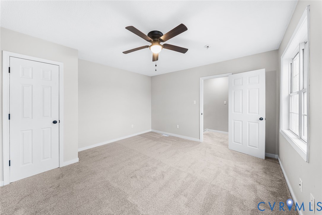 Neutral wall tones, wall-to-wall carpeting, multi-panel doors, and a ceiling fan with integrated lighting