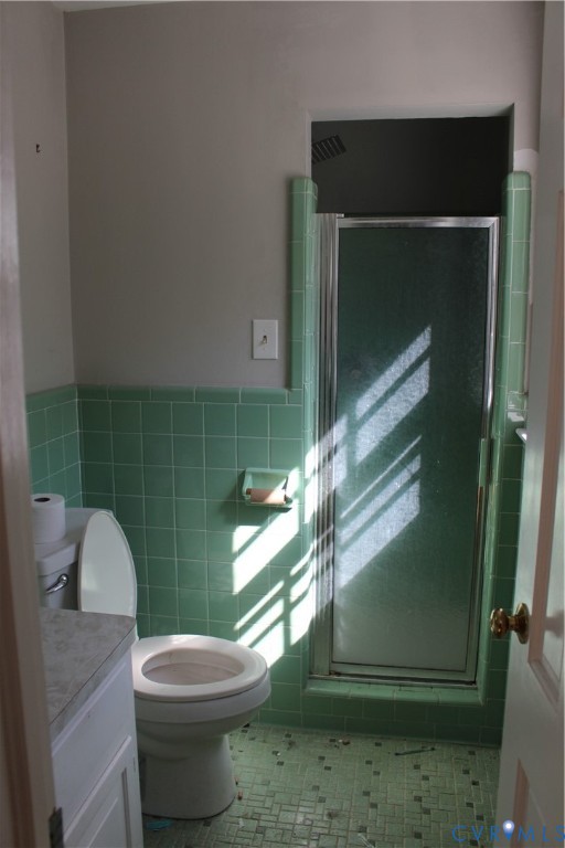 Bathroom featuring light green ceramic wall tiling, matching green tiled flooring, a built-in shower stall with a glass door, and an integrated recessed soap dish