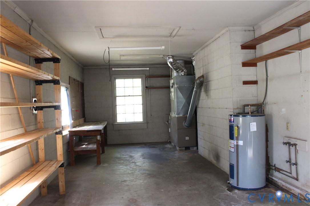 Utility space featuring exposed masonry walls, wooden wall-mounted shelving units, concrete flooring, a multi-pane window, and integrated heating and plumbing systems