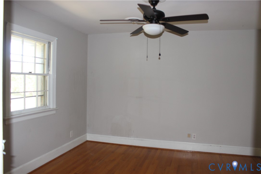 Room featuring wood-finish flooring, a double-hung window with grid pattern, and a black ceiling fan with an integrated light fixture