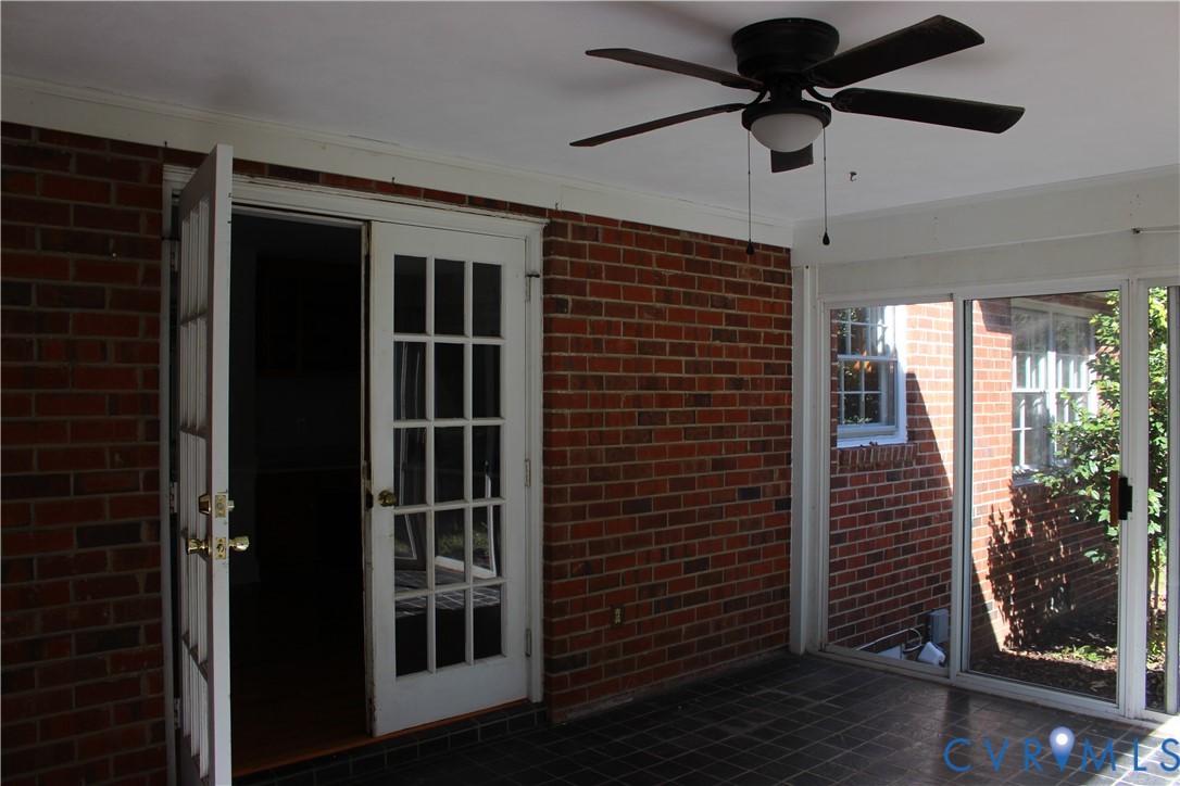 Covered patio featuring exposed brick walls, tile flooring, multi-pane glass doors, and a ceiling fan