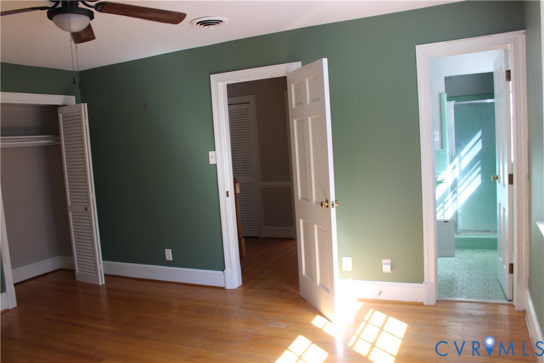 Interior room featuring wood-finish flooring, louvered-style closet doors, solid-core panel doors, and an attached ceiling fan with integrated lighting