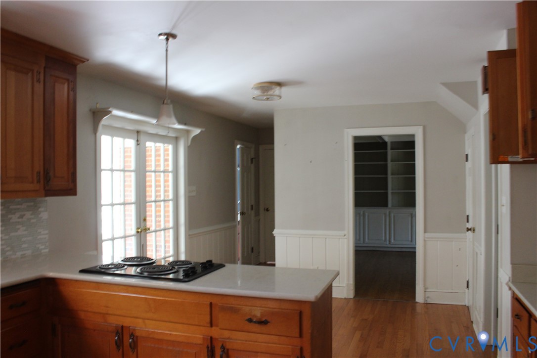 Kitchen featuring wood cabinetry, solid surface countertops, an integrated cooktop, beadboard wainscoting, and wood-finish flooring