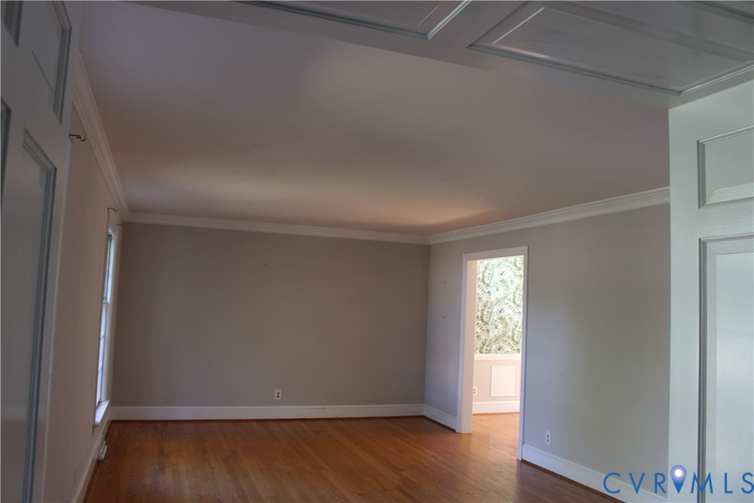 Room featuring wood-finish flooring, crown molding, and wainscoting paneling details on the ceiling