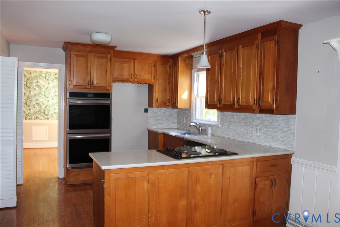 Kitchen featuring wood cabinetry, integrated double wall ovens, a cooktop, stone-finish countertops, and a textured tile backsplash