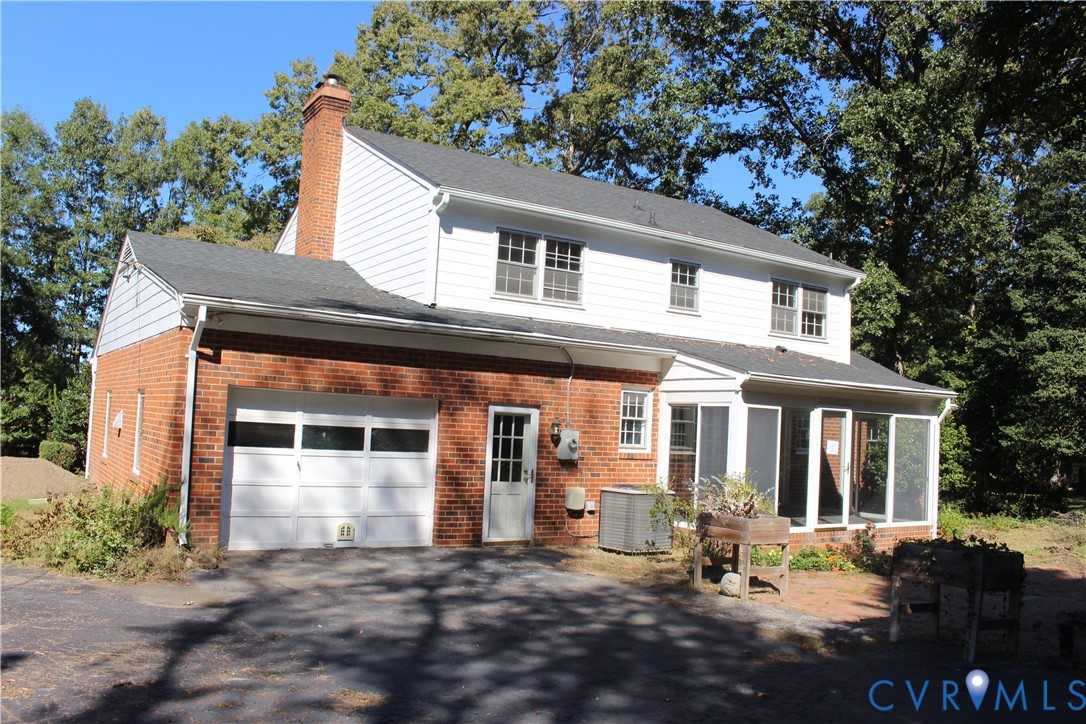 Exterior featuring a combination of red brick and white horizontal siding, an attached garage, a brick chimney, and a screened-in porch