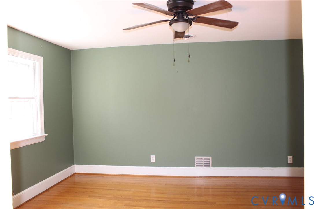 Room featuring wood-finish flooring, a multi-blade ceiling fan with integrated lighting, and a single-pane window