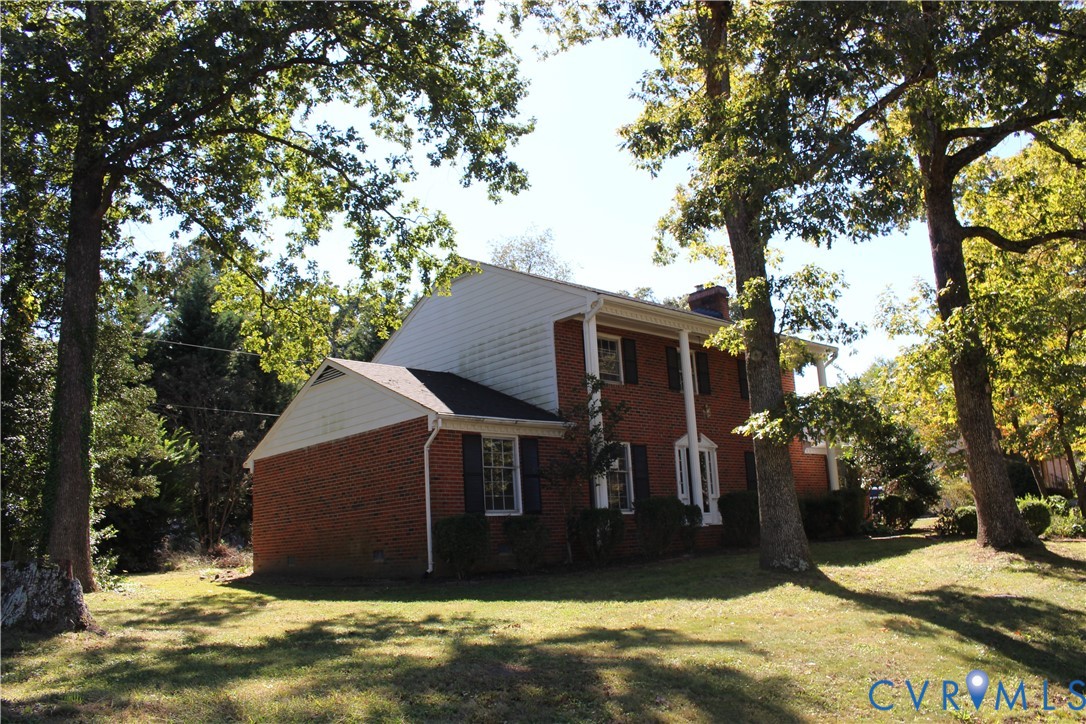 Two-story exterior featuring a brick and horizontal siding facade, a covered porch with columns, and shuttered windows, situated on a lot with mature trees