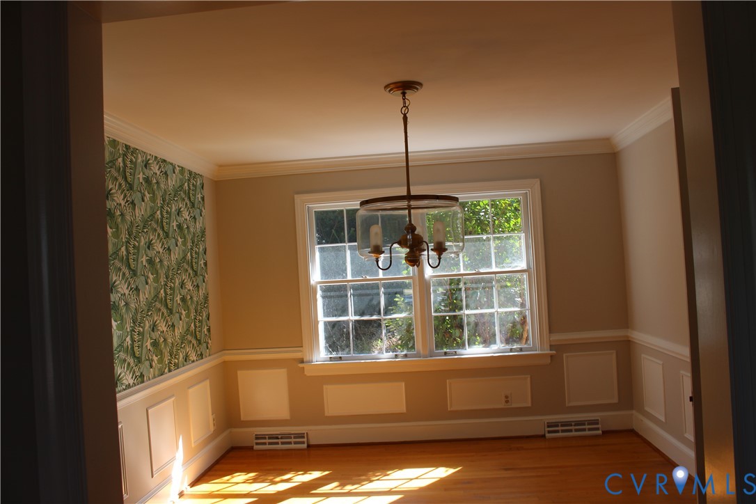 Room featuring wood-finish flooring, wainscoting, crown molding, a multi-pane window, and a drum-style pendant light fixture