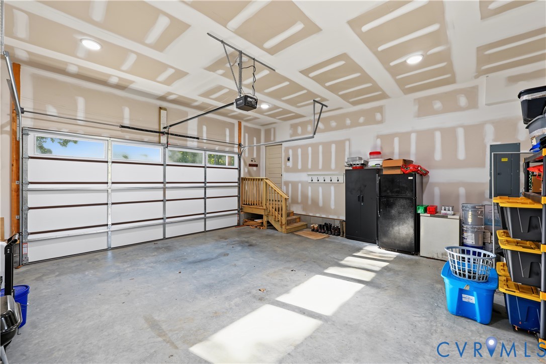 Multi-car garage featuring a sectional door with windows, concrete flooring, recessed lighting, and wooden stair access to the residence